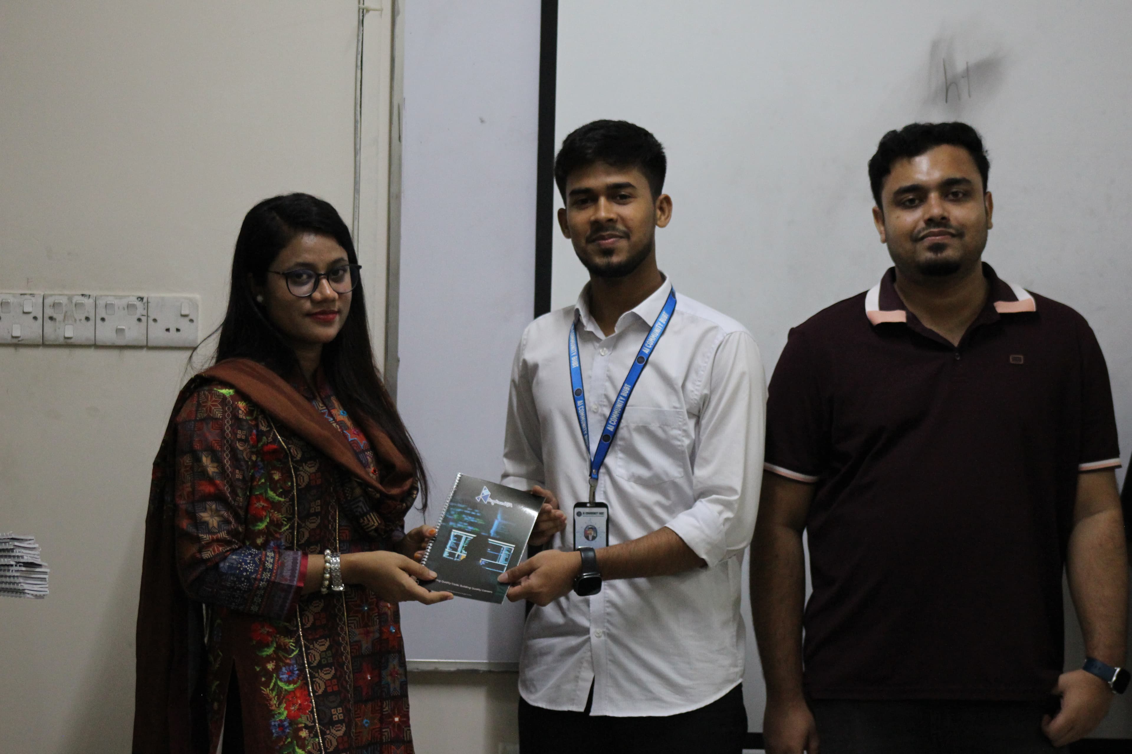 A BUBT student receiving a BugBoundQA notebook from the trainer at the end of the session.