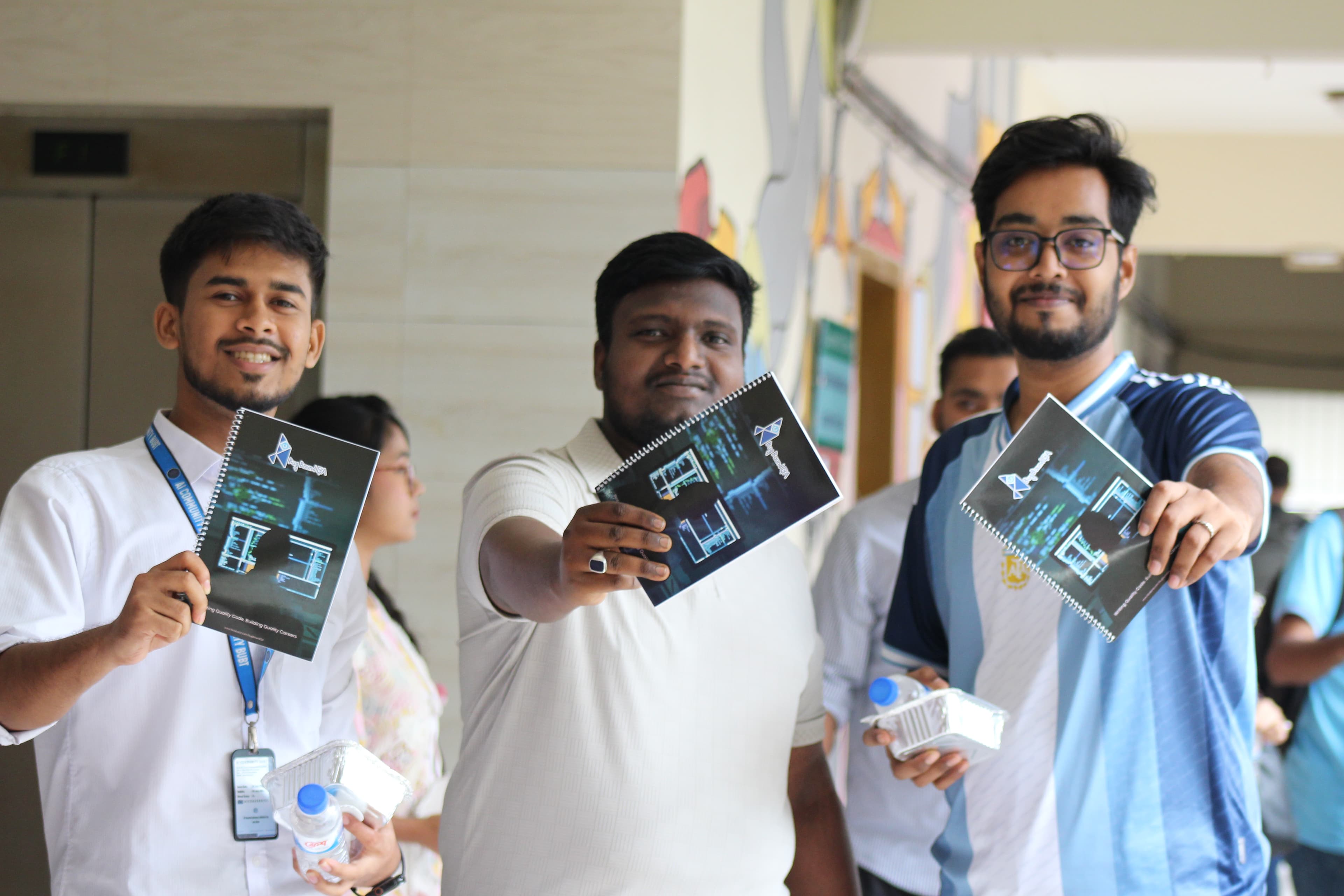 Three BUBT students smiling and holding up the BugBoundQA notebooks they received for completing the workshop.